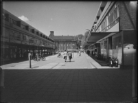L-1956 Winkelend publiek op de Nieuwemarkt. Links en rechts winkels met bovenwoningen. Op de achtergrond de ...