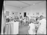 L-2809 Docent (links) met leerlingen in een klaslokaal van een kleuterschool aan de Ameidestraat.