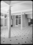 L-3073 Hal van een school aan de Larikslaan met betegelde vloer, zuilen met keramiek en glas-in-lood ramen.