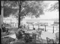 L-3449 Een man, vrouw en kind zitten op het terras van café Bellevue aan de Parkkade. Op de achtergrond varen ...