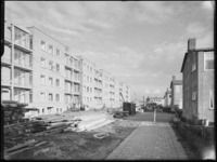 L-3864 Bouw van een flatgebouw aan de Oldegaarde. Op de voorgrond liggen steigerplanken en houten palen. Tegen de gevel ...