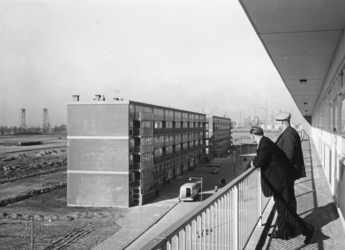 L-5037 Twee mannen staan op een galerij van een flatgebouw aan de Wijnruitstraat in Hoogvliet. Op de achtergrond links ...
