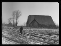 L-5087 Een man loopt door het besneeuwde boerenland voor een boerderijen aan de Beer in Europoort-Oost.