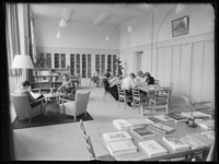 L-544 Leerlingen en docenten lezen boeken in een bibliotheek. Op de voorgrond een tafel met boeken, op de achtergrond ...