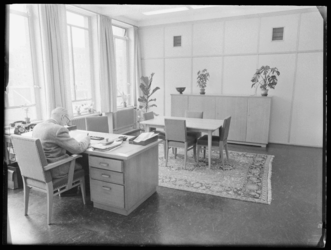 L-694 Ambtenaar zit achter zijn bureau op een kantoor in het Stadstimmerhuis aan het Haagseveer.