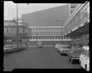 L-8409 De Kruiskade met uitkijk op de het concertgebouw De Doelen in aanbouw met geparkeerde auto's en winkels.