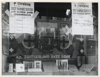 1977-3192 Een etalage van een zuivelhandel met aankondigingen van het beschikbaar stellen door het Rode Kruis van ...