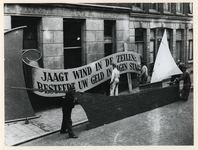 1977-3522 Bij het stadhuis wordt gewerkt aan een model van een zeilschip met het opschrift: Jaagt wind in de zeilen: ...
