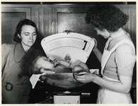 1977-3679 Een verpleegkundige van de GGD (Gemeentelijke Geneeskundige Dienst) weegt een baby, tijdens de ...