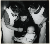 1977-3681 Verpleegkundigen van de GGD (Gemeentelijke Geneeskundige Dienst) verstrekken vitamine D aan een baby, tijdens ...