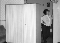 14-03 Een dame kijkt door een deur van een woning in de Haarlemmerstraat. Tegen de muur is krantenpapier geplakt.